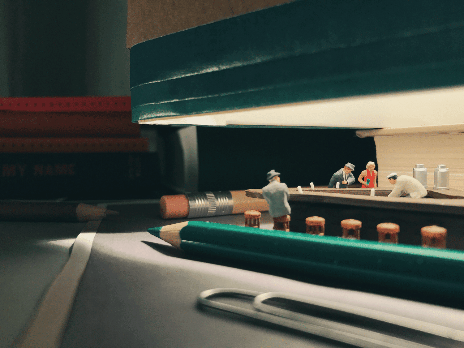 Photographie miniature de petits personnages entre des livres et des crayons par Derrick Lin