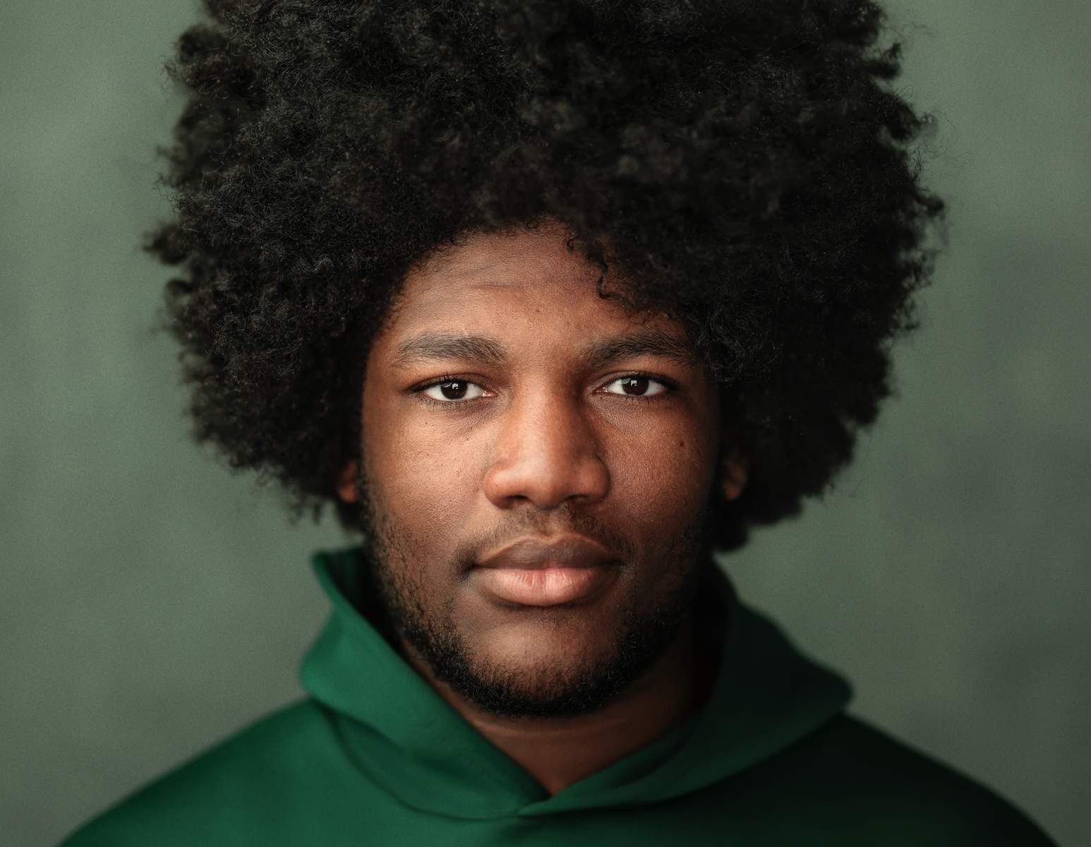Studio headshot photography of a young man in a green hoodie with natural light and a soft green background.