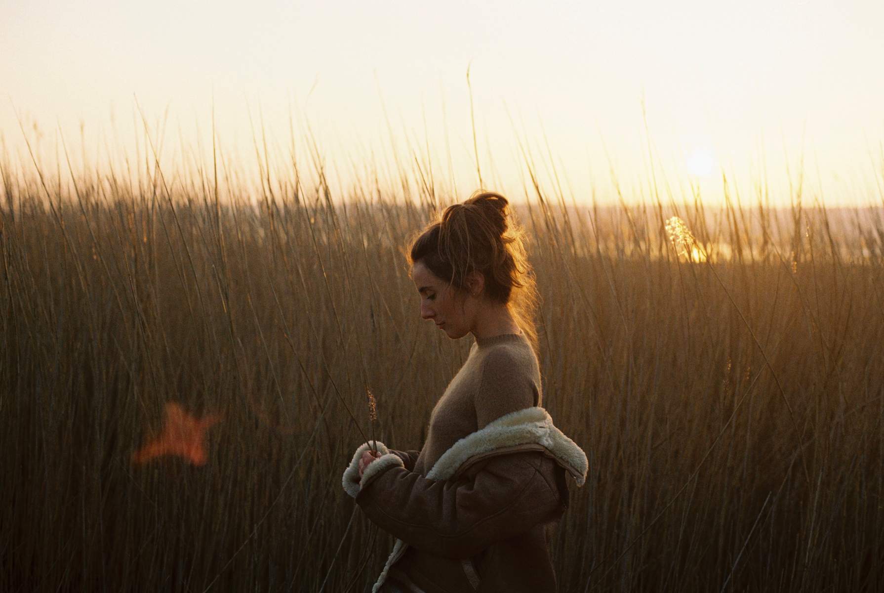 Woman standing among tall grasses at golden hour with warm backlighting, photographed by Lena Jeanne.