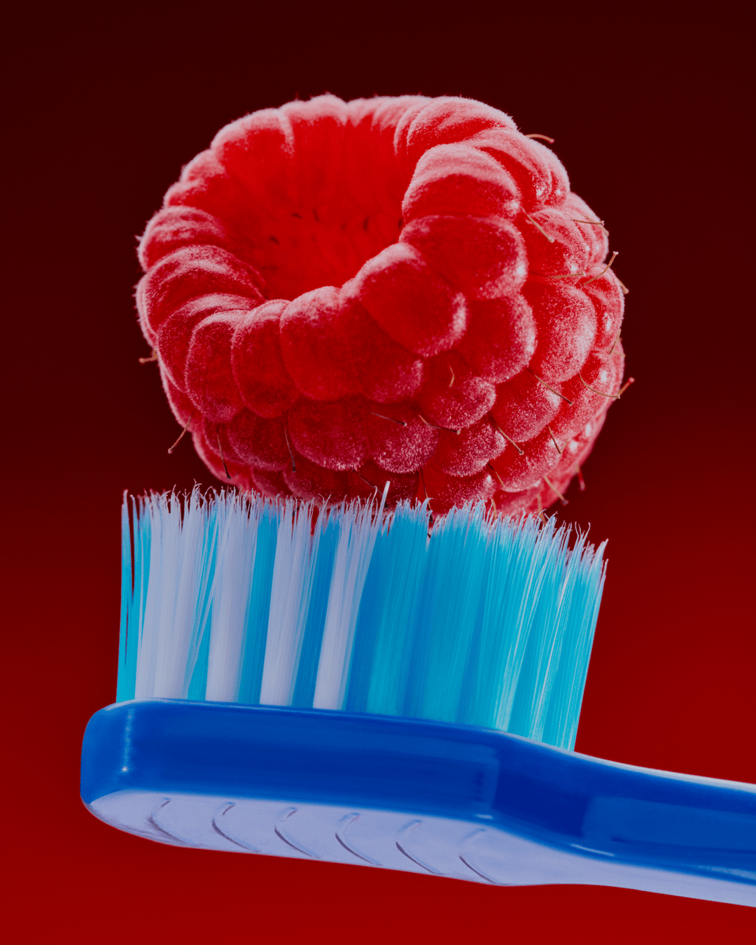 A raspberry balanced on a toothbrush head, against a deep red background.