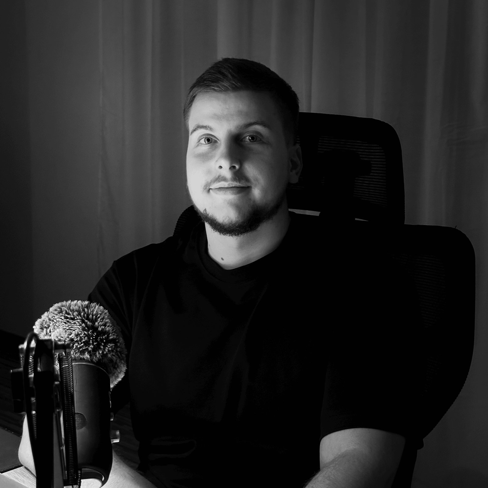 Black and white portrait of brand designer Ren Barkevics seated at a desk beside a microphone, looking toward the camera.